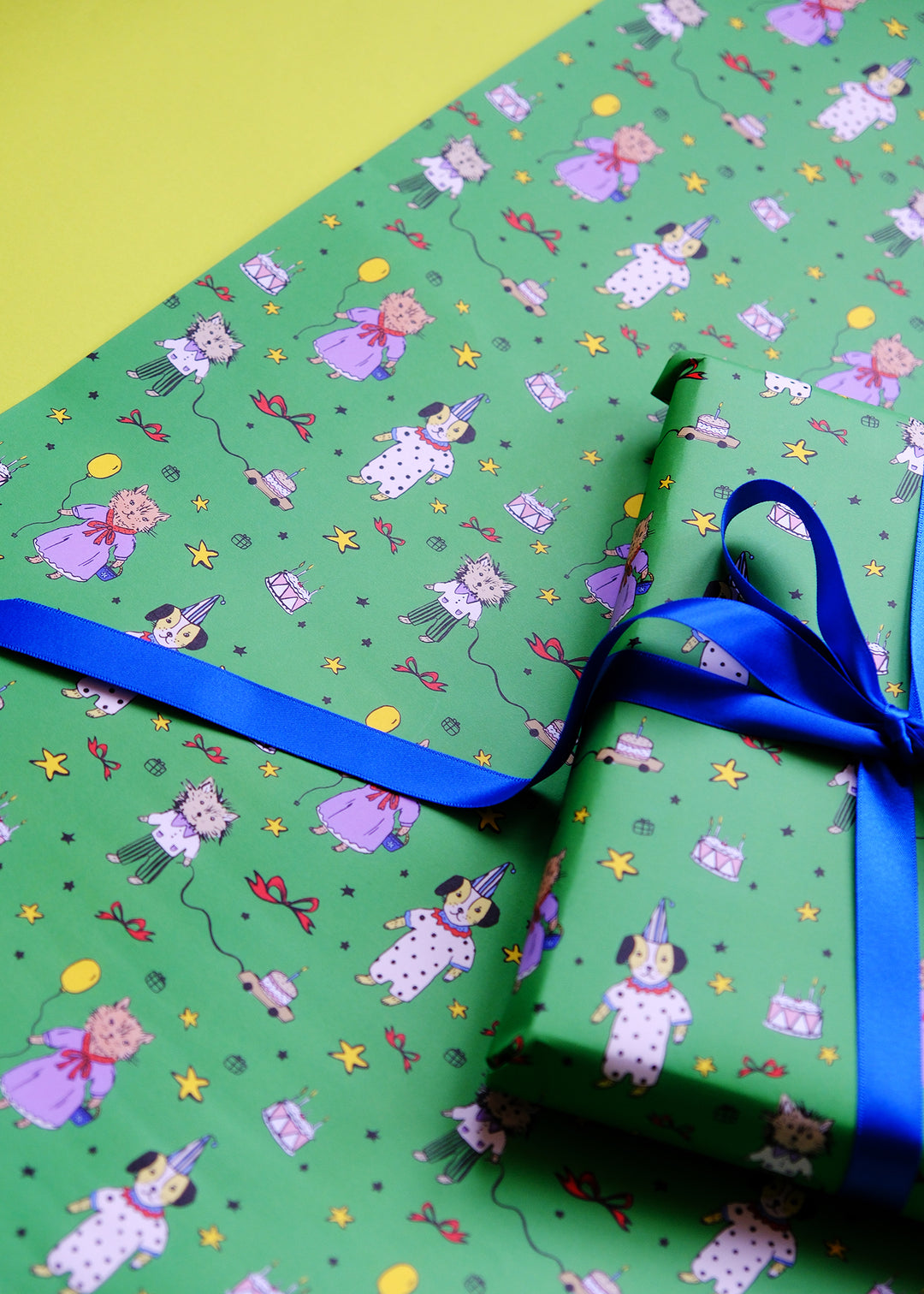Gift wrapped in green paper with cartoon dog and cat characters and a blue ribbon on a yellow background