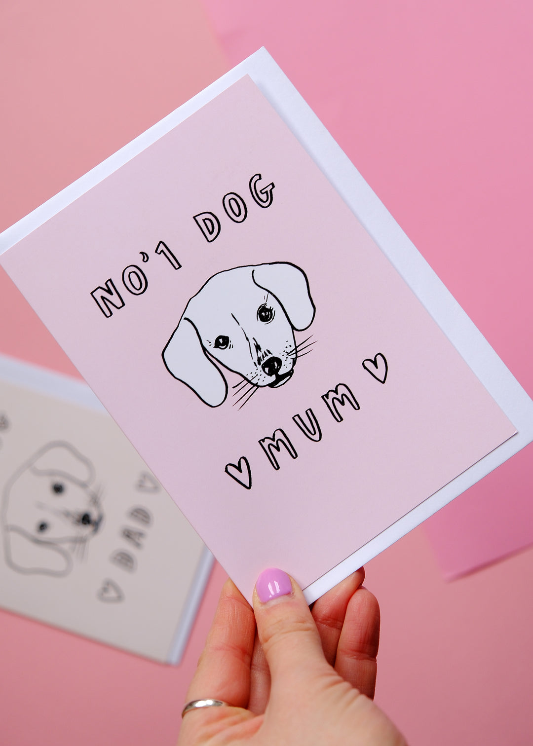 Card with a dog illustration and text 'No 1 Dog Mum' held by a hand on a pink background